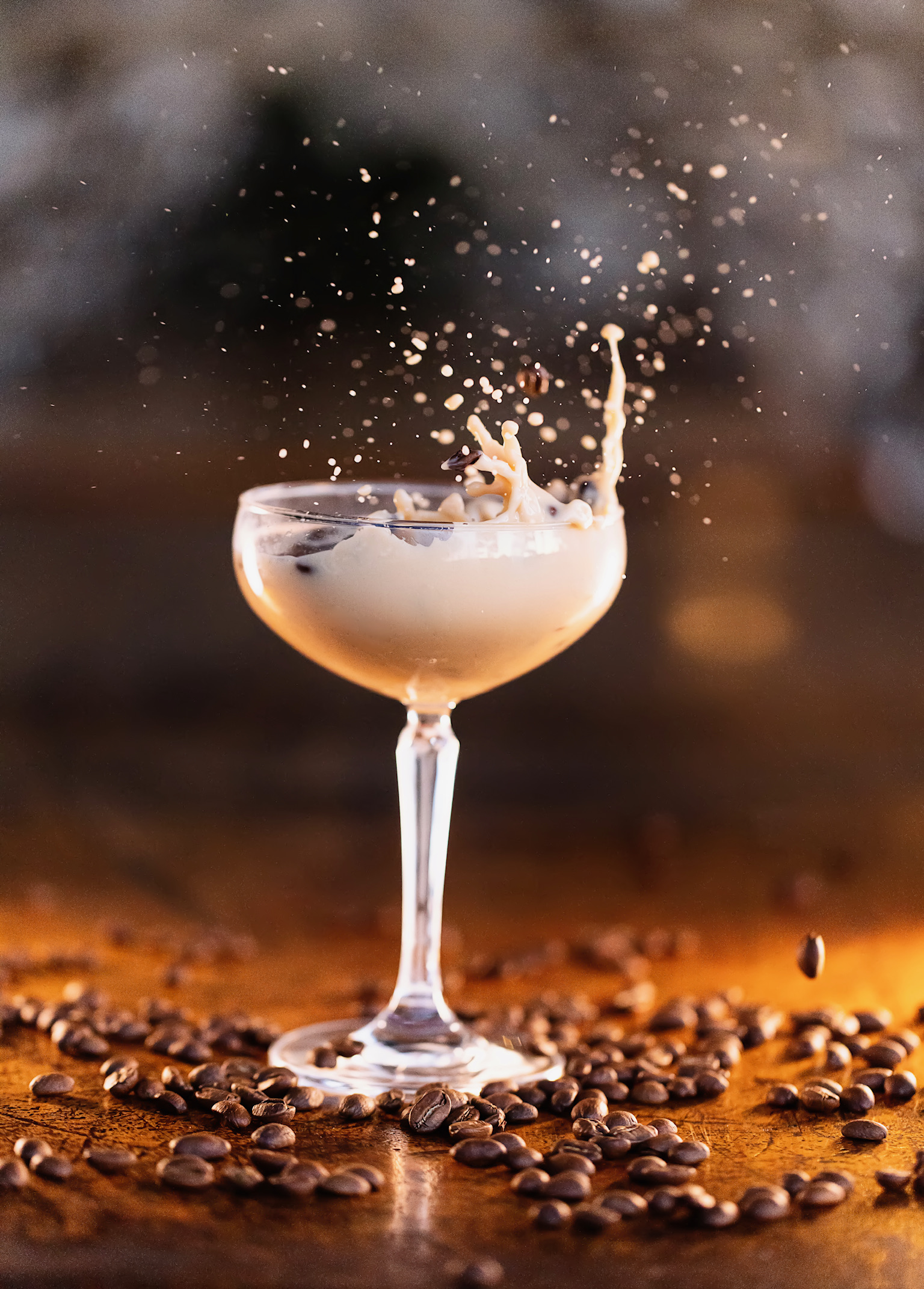 Creamy espresso cocktail in a coupe glass with coffee splashing upward, surrounded by roasted coffee beans on a wooden table at Old Florida Fish House.