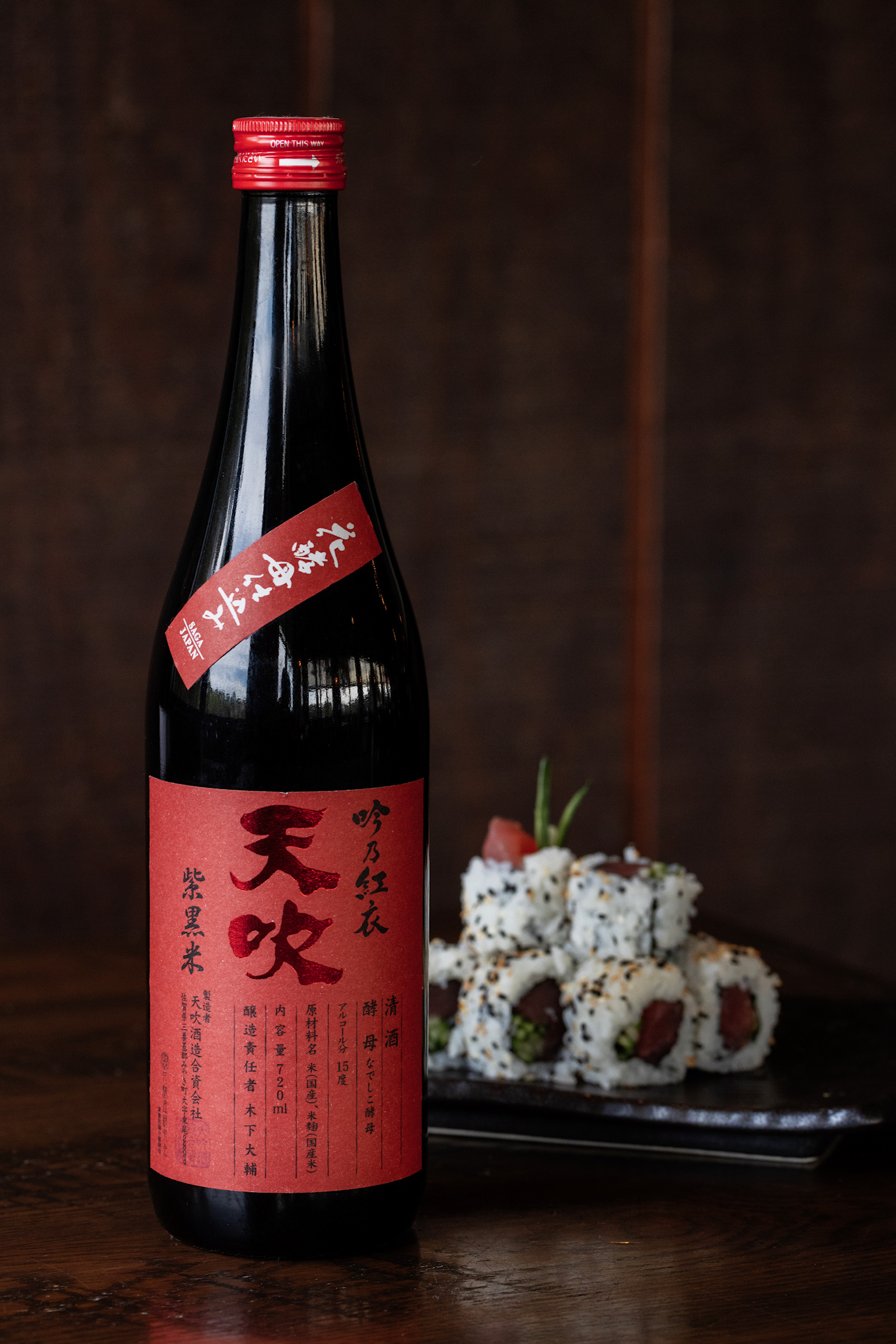 Bottle of premium sake displayed on a wooden table with sesame-crusted tuna sushi rolls in the background at Old Florida Fish House.