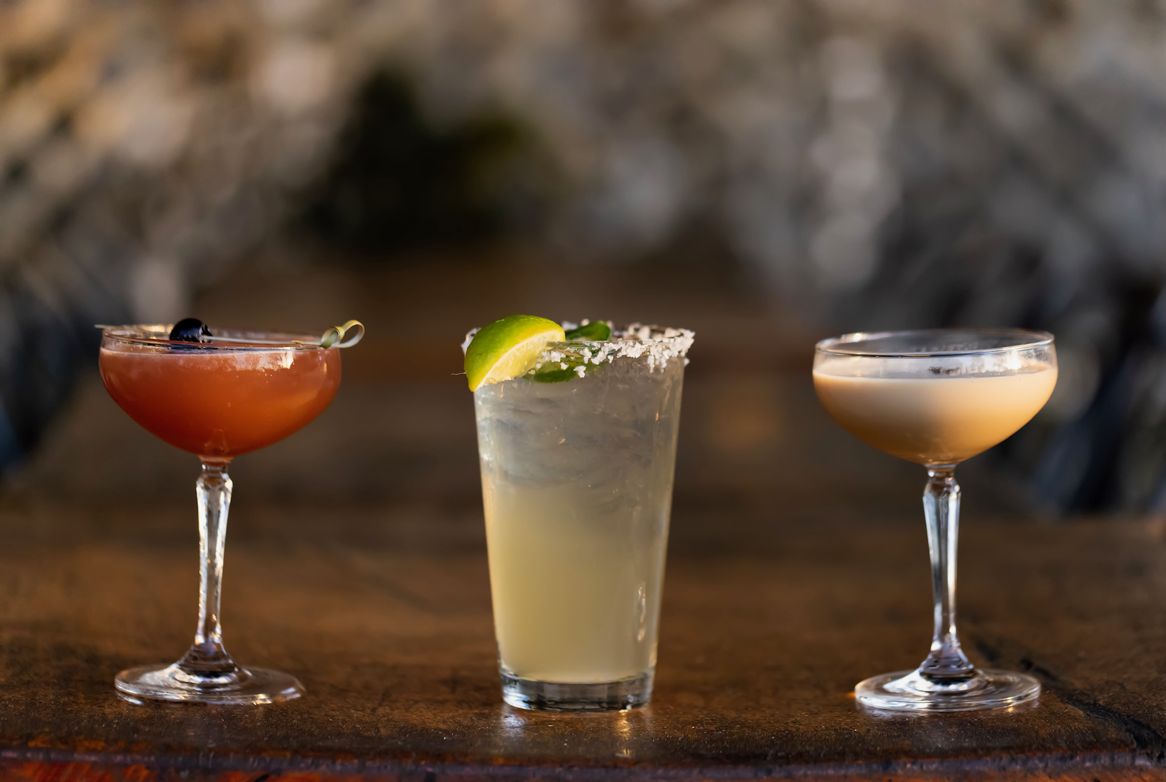 Three handcrafted cocktails, including a cherry-garnished coupe cocktail, a salted lime cocktail over ice, and a creamy espresso-style cocktail, served on a wooden table at Old Florida Fish House.