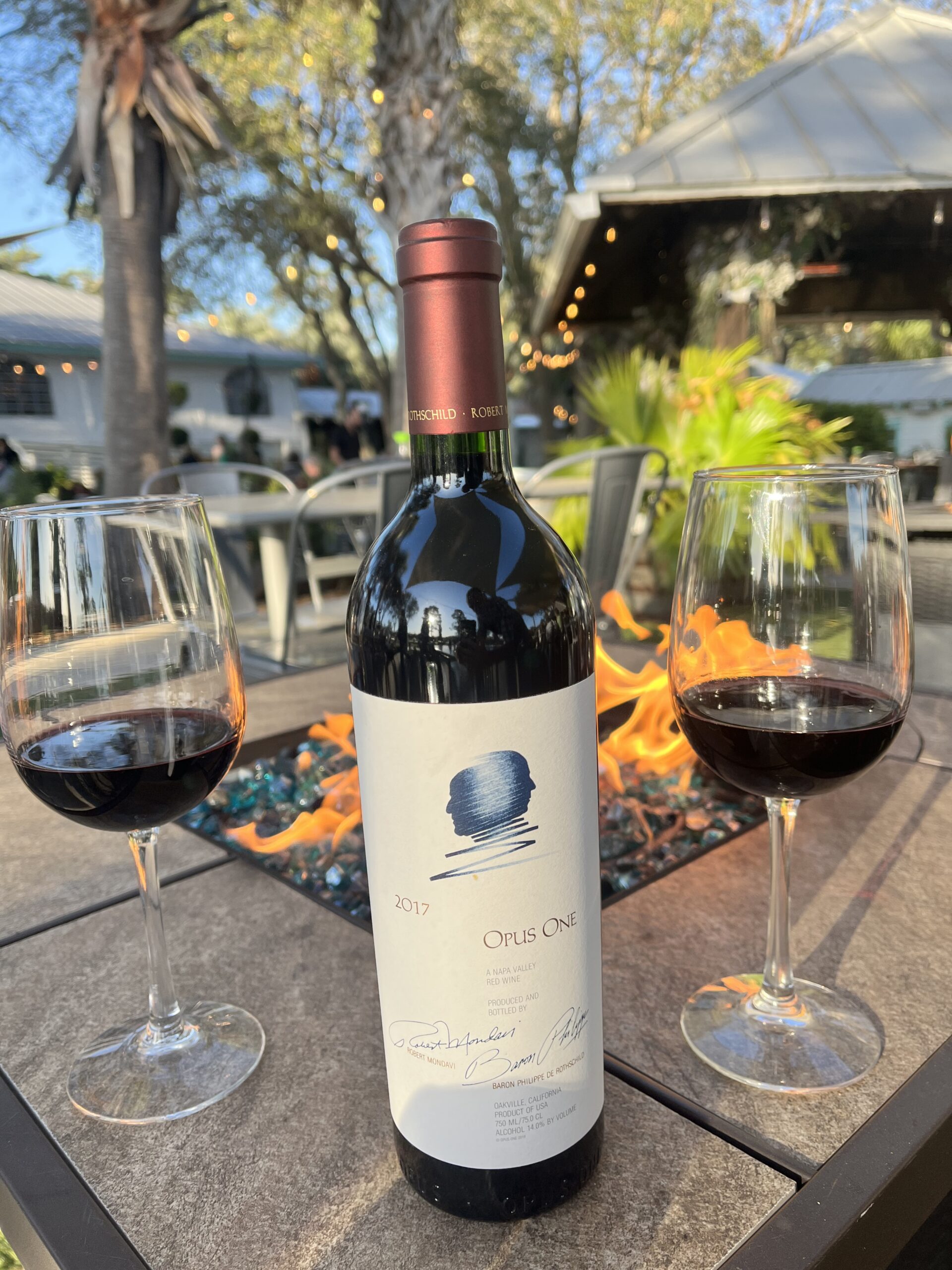 Bottle of 2017 Opus One Napa Valley red wine with two glasses by the outdoor fire table at Old Florida Fish House.