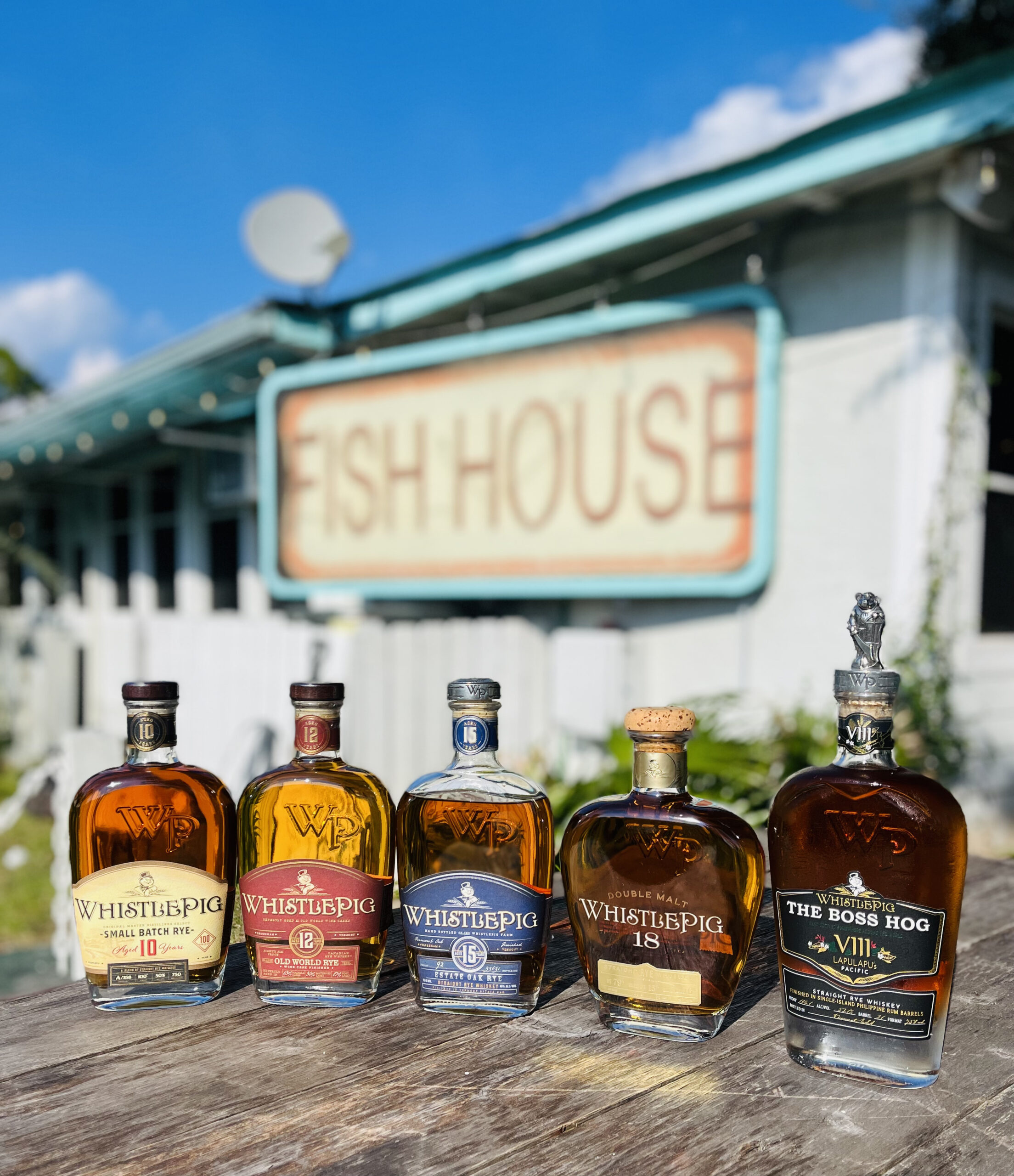 Collection of premium WhistlePig rye whiskey bottles, including 10 Year, 12 Year, 15 Year, 18 Year Double Malt, and Boss Hog VIII, displayed on a rustic wooden table at Old Florida Fish House.